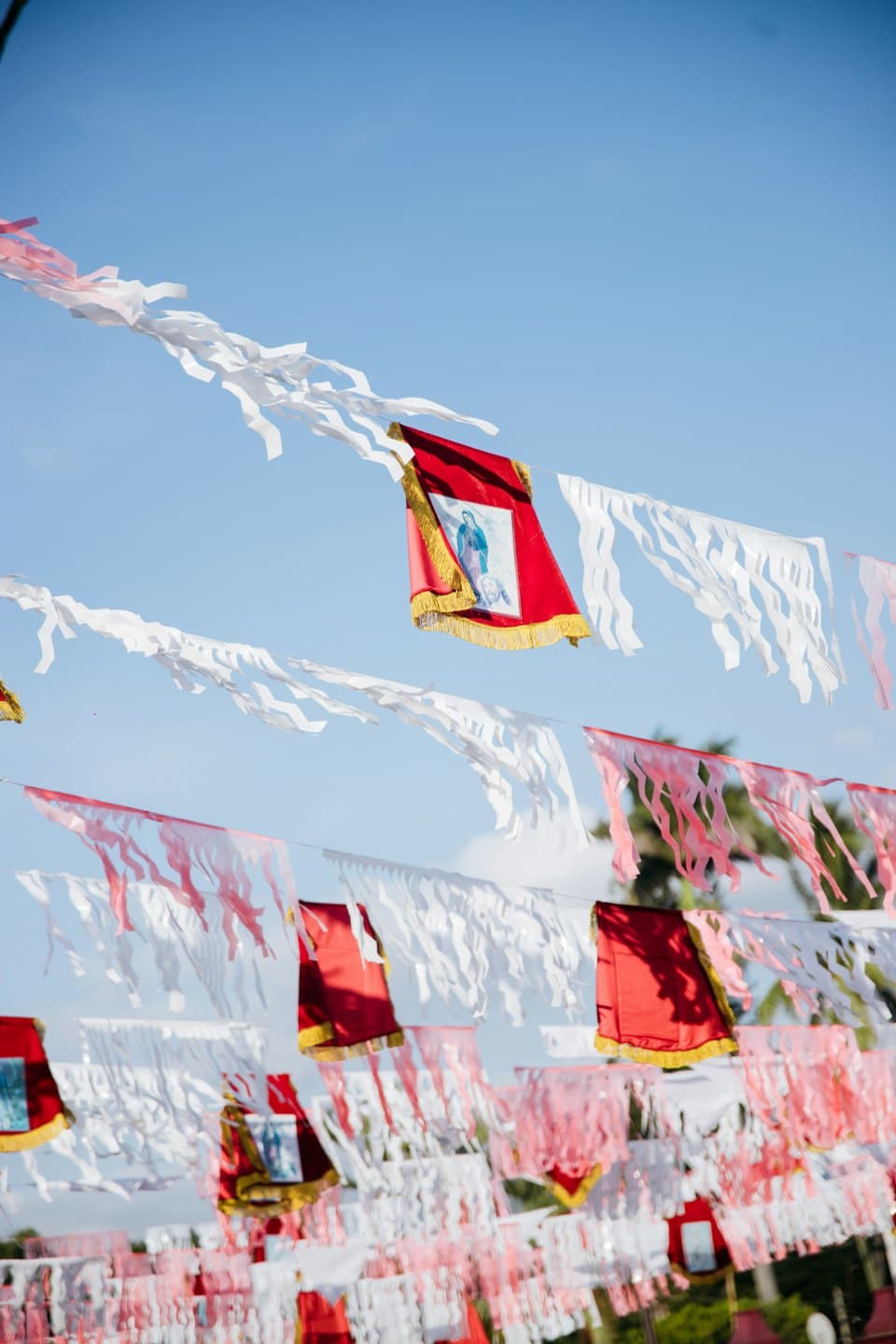 Dekorative Girlanden und rote religiöse Banner hängen vor blauem Himmel.